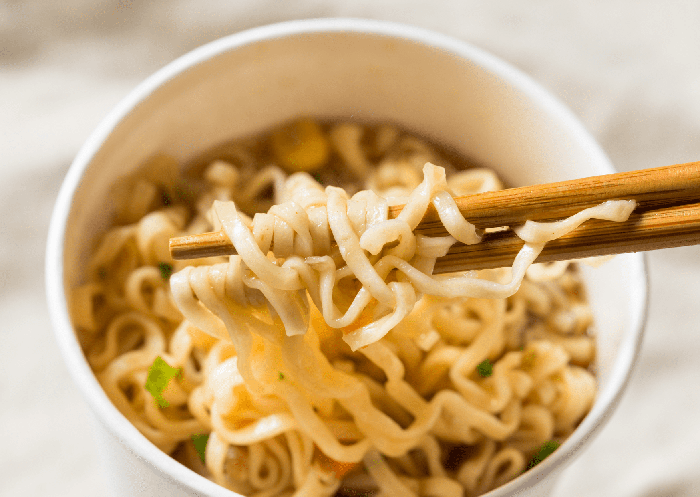 Fideos ramen asiáticos levantados con palillos en un cuenco de caldo.